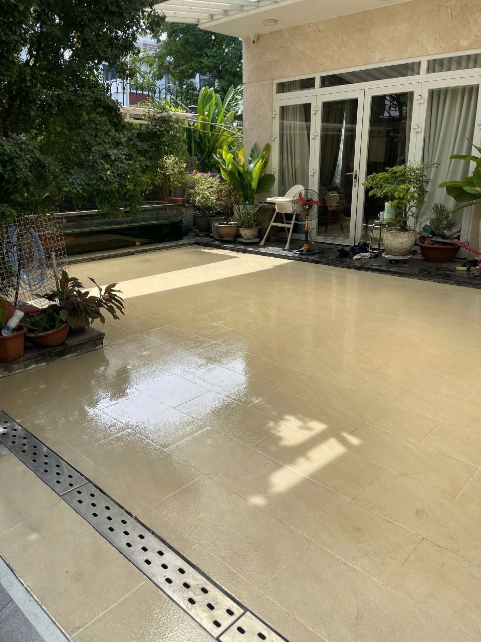 Sân vườn nhà ở lát gạch men màu kem được phủ lớp trong suốt bóng, có rãnh thoát nước inox