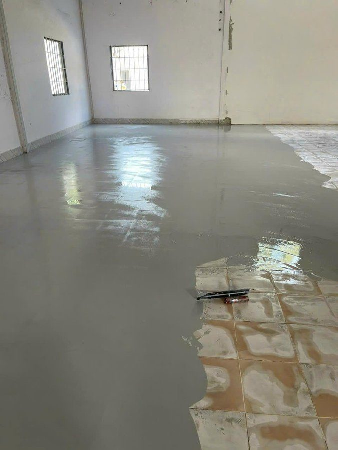 Sơn epoxy tự san phẳng đang chảy phủ kín nền gạch men vàng nâu — cây gạt chuyên dụng