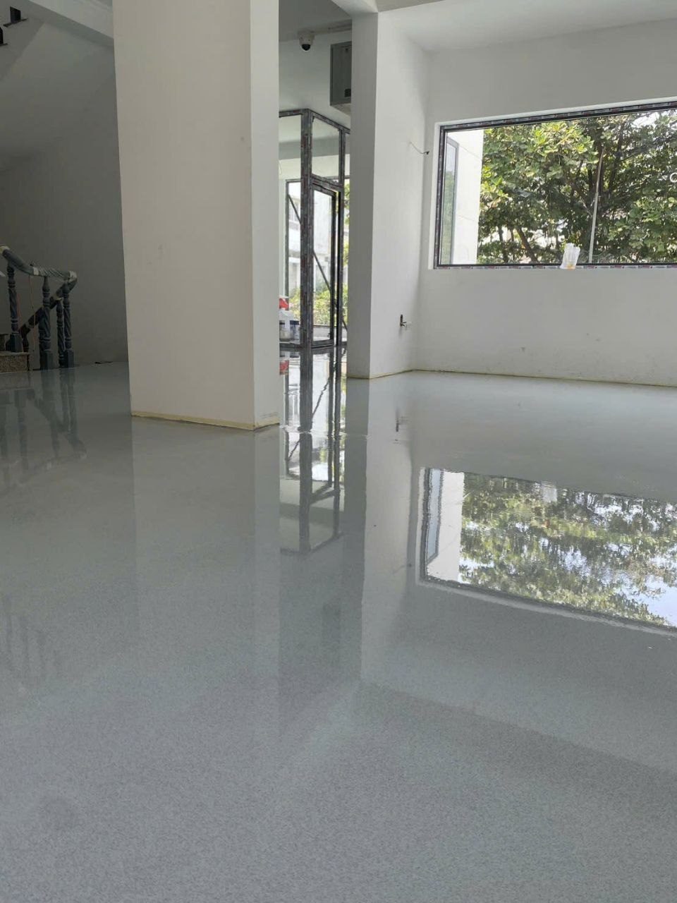 Sàn nhà phố sơn epoxy tự san phẳng giả đá màu xám sáng bóng gương phản chiếu cửa sổ và cây xanh