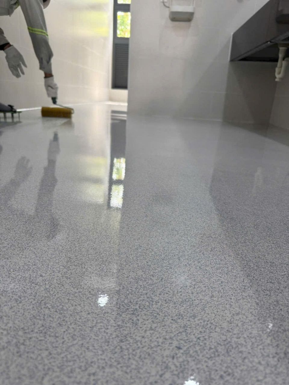 Thợ thi công lăn lớp topcoat trong suốt lên sàn epoxy giả đá xám xanh trong nhà bếp