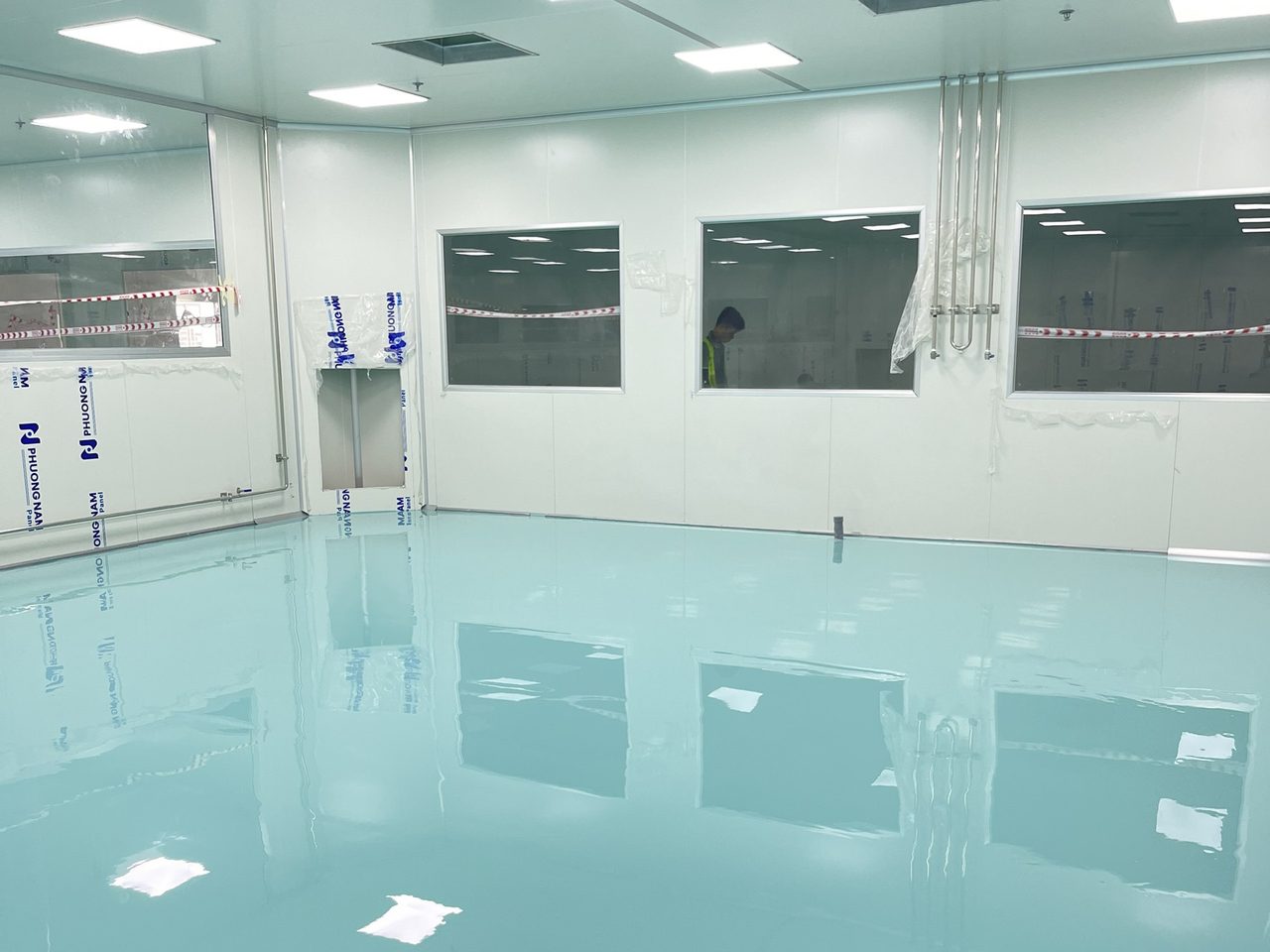 Phòng sạch với sàn epoxy tự phẳng màu xanh mint bóng gương, tường panel và hệ lọc khí HEPA trên trần