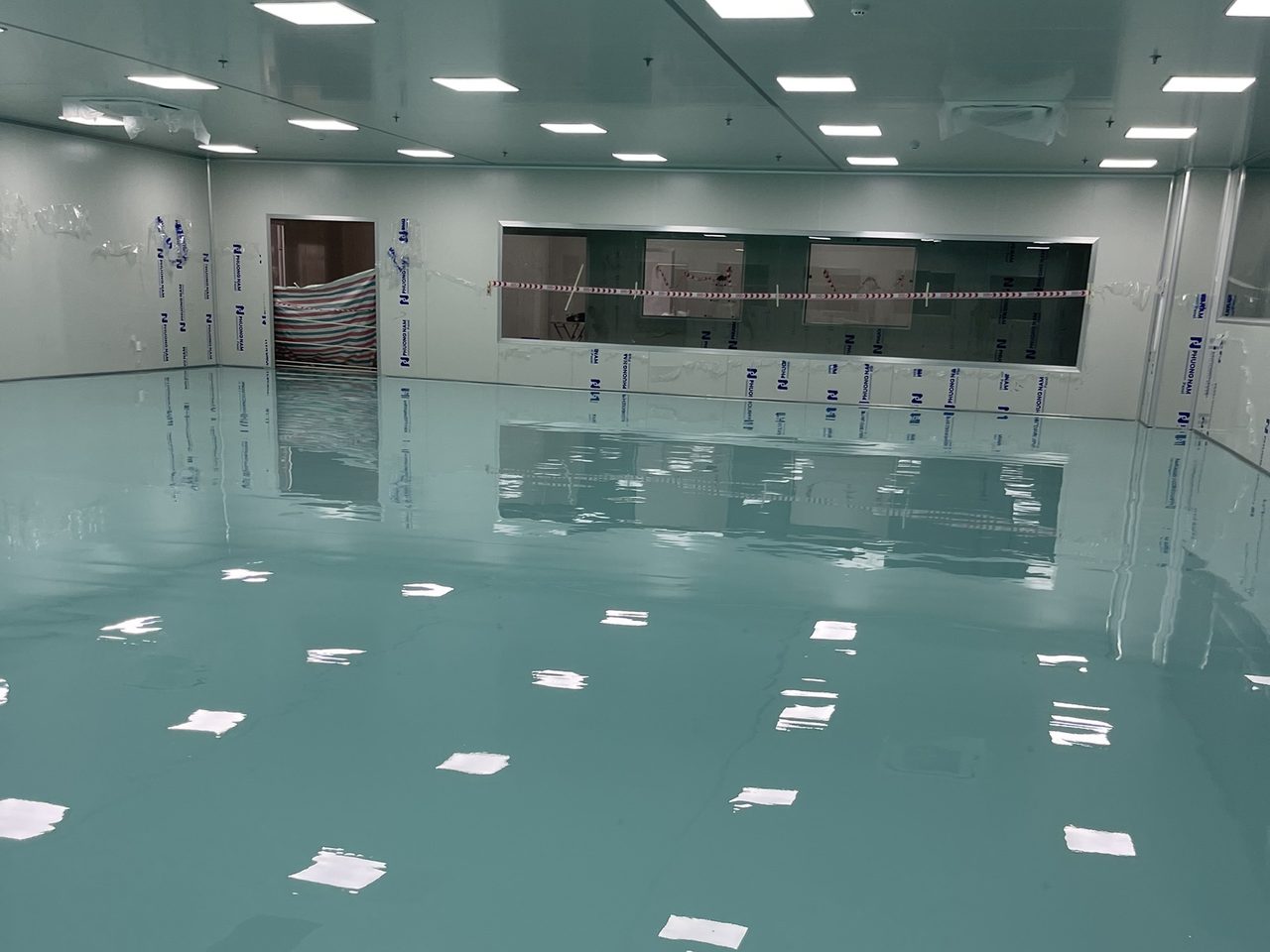 Phòng sạch diện tích lớn với sàn epoxy tự phẳng xanh mint và tường panel còn màng bảo vệ