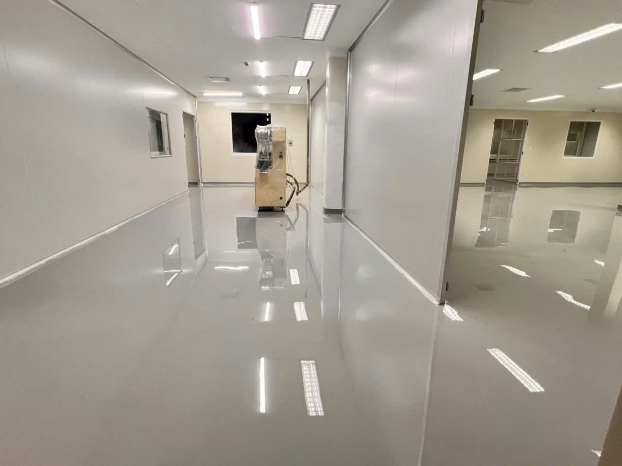 Hành lang nhà máy với sàn epoxy tự phẳng bóng liền khối và chân tường bo cong màu xám