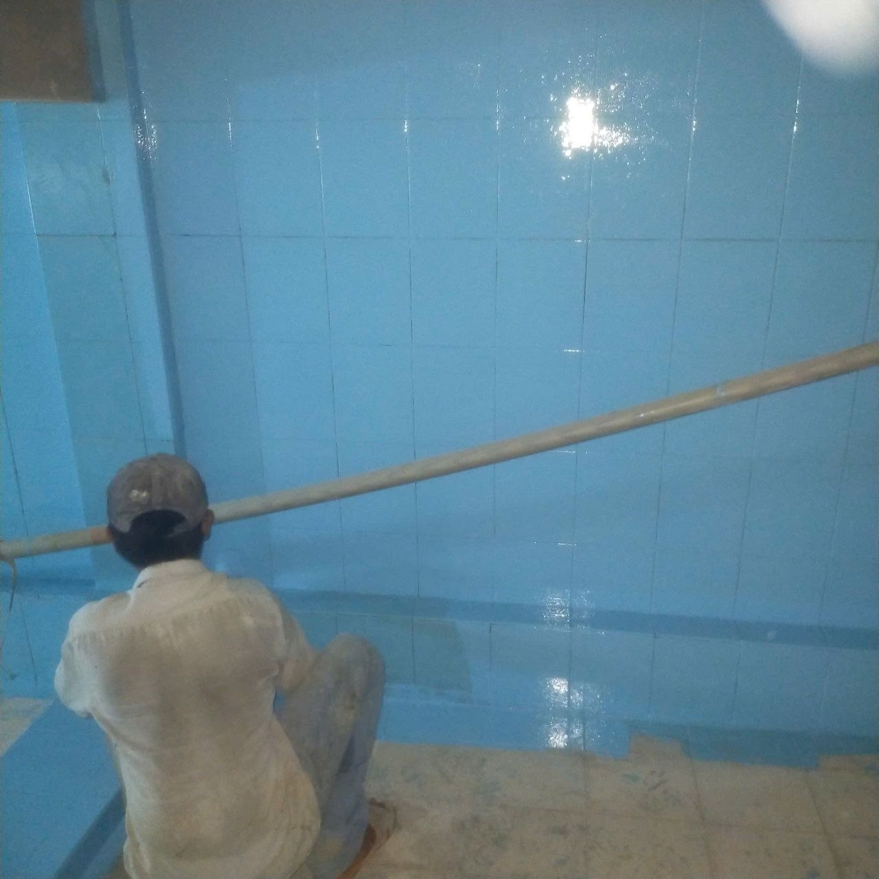 Công nhân dùng cây lăn nối dài thi công sơn epoxy lên thành hồ nước sinh hoạt ngầm ốp gạch men