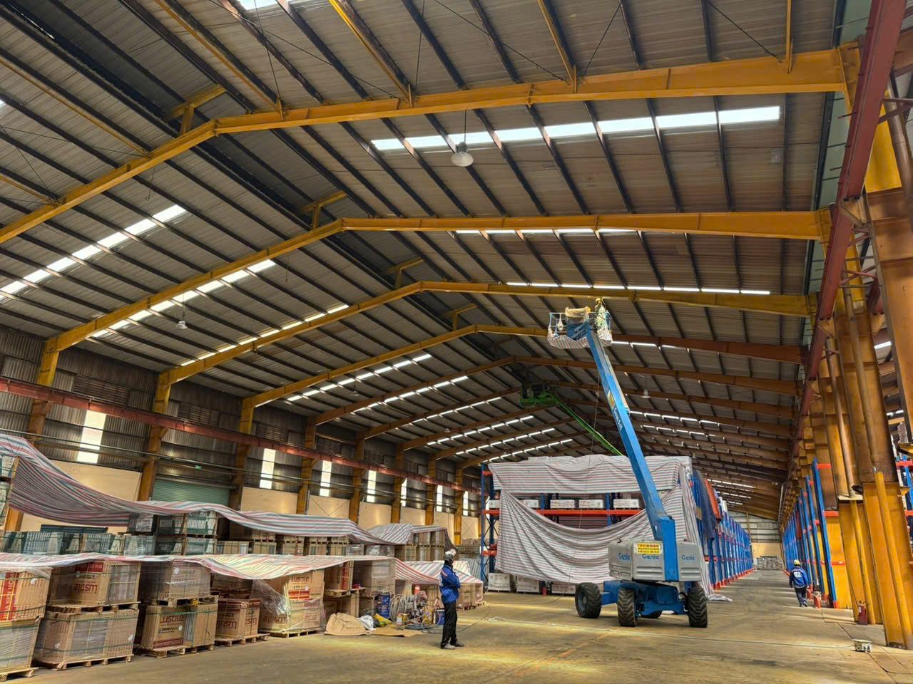 Thi công sơn bảo trì khung thép mái nhà kho đang vận hành, hàng hóa được che bạt bảo vệ