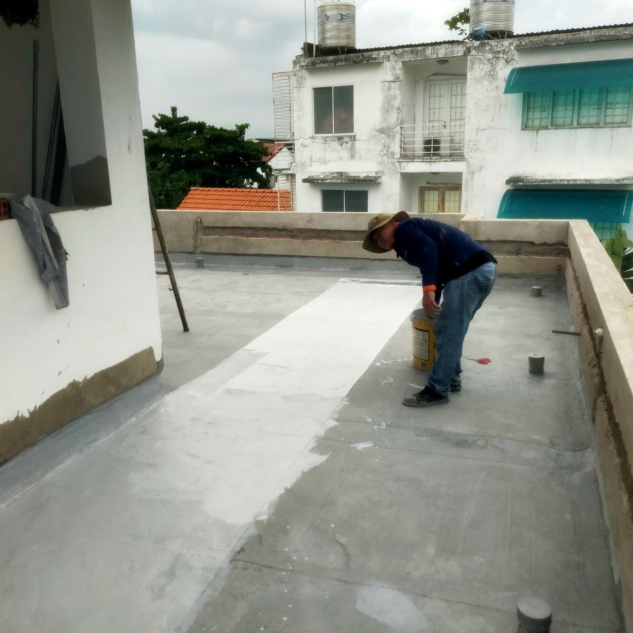 Thợ thi công lớp chống thấm theo dải trên sân thượng bê tông, dải lưới trắng đã trải sẵn