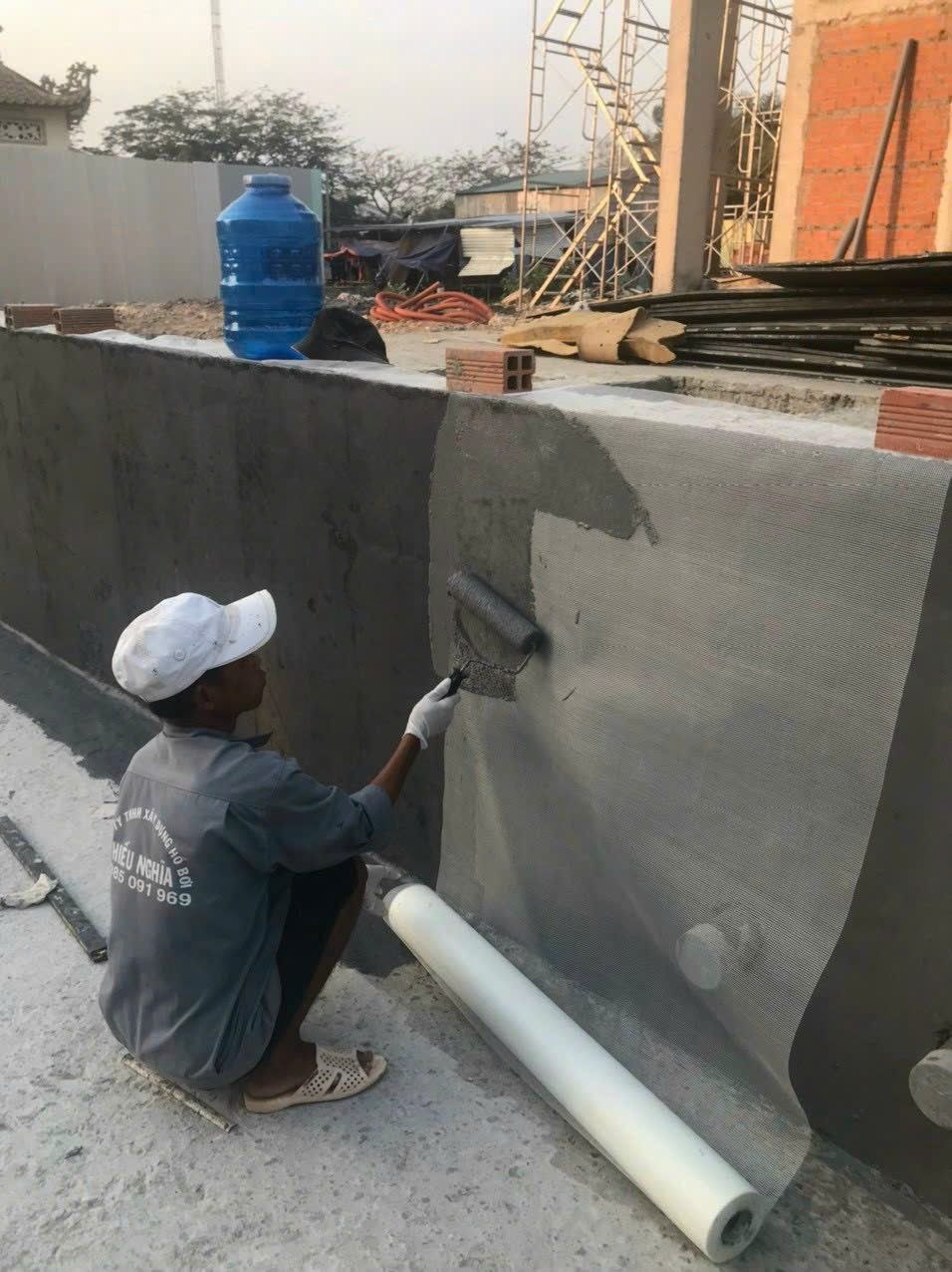 Công nhân lăn lớp chống thấm lên lưới gia cường đã dán trên tường bê tông, cuộn lưới dựng bên cạnh