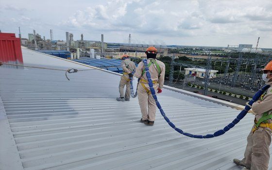 Toàn cảnh đội thi công phun polyurea trên mái tôn dốc nhà máy với đầy đủ thiết bị an toàn