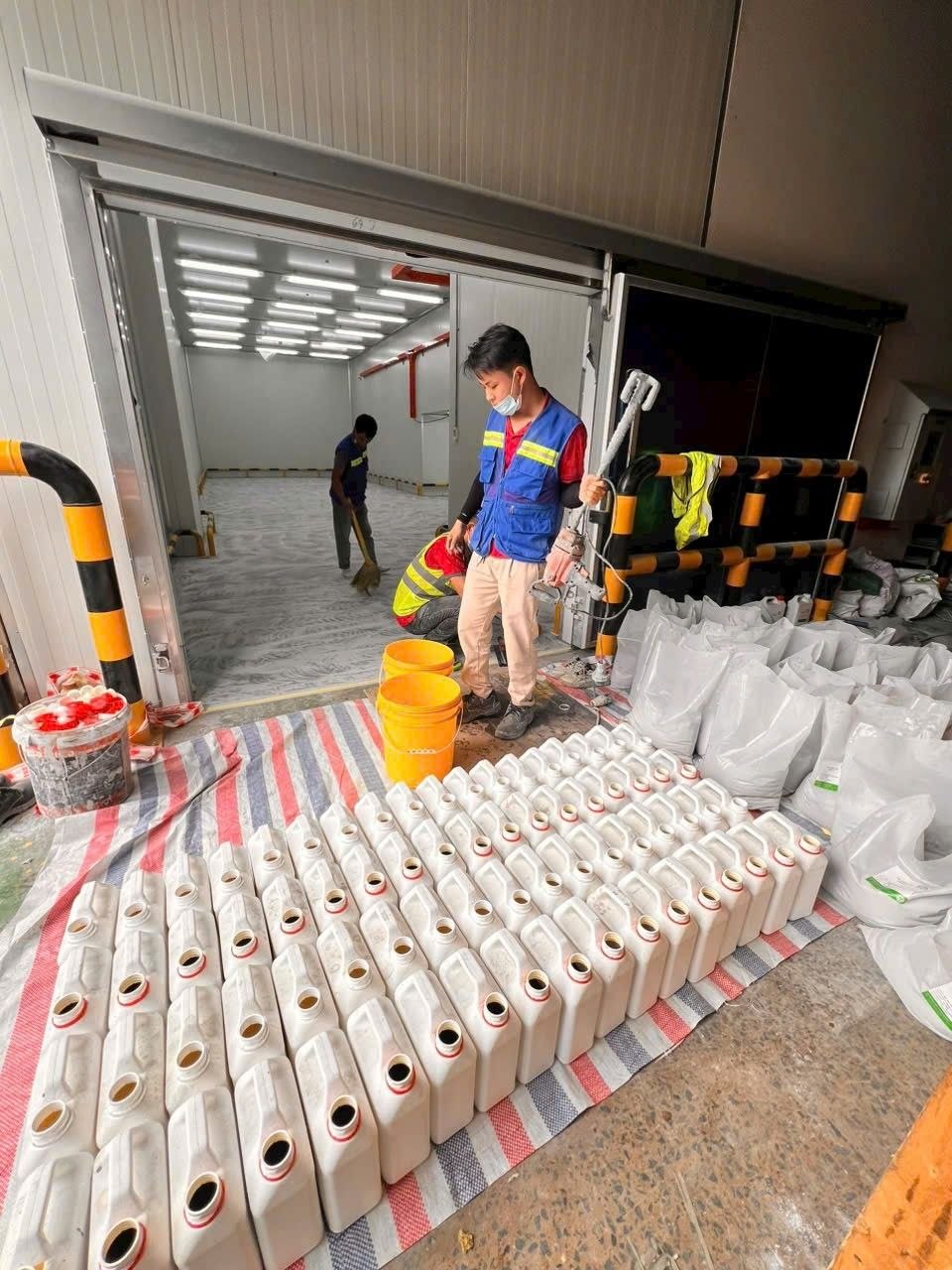 Tập kết vật tư vữa PU: can thành phần lỏng và bao bột cốt liệu xếp sẵn ngoài cửa phòng trước khi thi công
