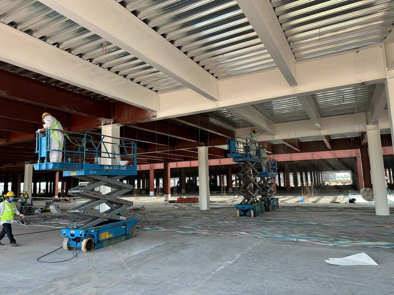Thi công sơn kết cấu thép nhà xưởng nhiều tầng bằng xe nâng người, cột đã sơn lót đỏ và dầm đã phủ hoàn thiện màu trắng