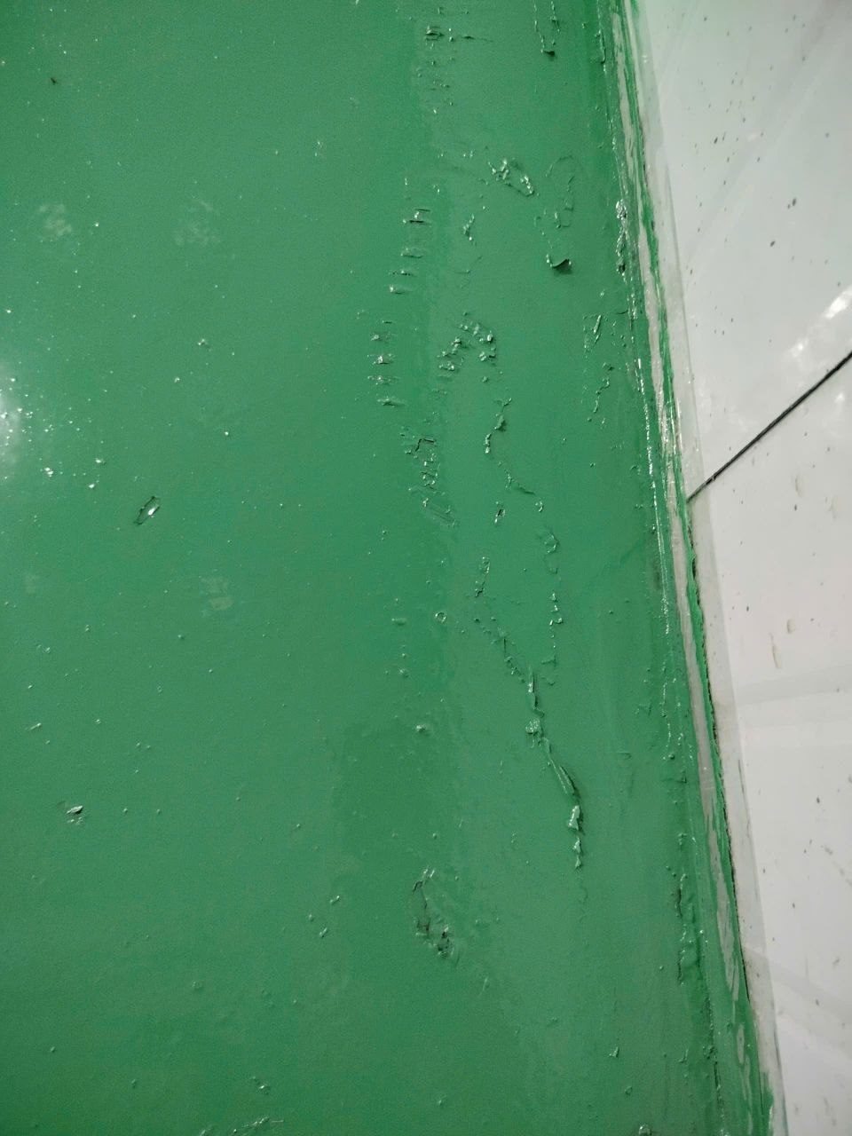 Chân tường epoxy xanh bị rộp nhăn do lớp sơn cũ bên dưới trương nở khi gặp dung môi sơn mới
