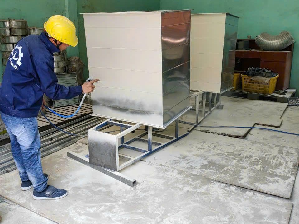 Thợ đội mũ bảo hộ vàng phun sơn kem lên hộp gió tôn kẽm tại xưởng gia công