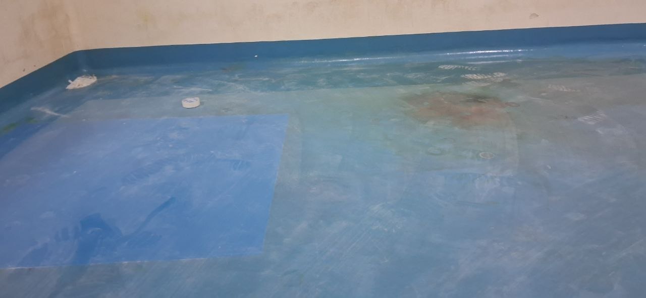 Sàn epoxy tự phẳng màu xanh bị vàng loang lổ do hóa chất, có vết ố nâu đỏ và vùng bạc màu
