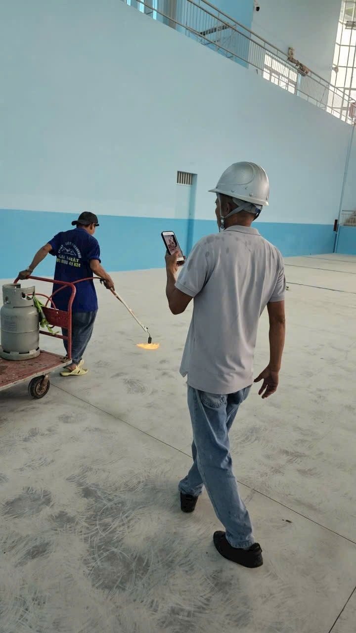Thợ dùng đèn khò gas xử lý ẩm nền bê tông sát chân tường trước khi sơn epoxy - kỹ sư giám sát ghi hình