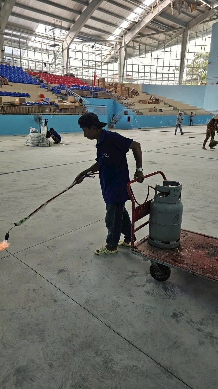 Thợ khò nền bê tông toàn bộ mặt sàn nhà thi đấu bằng đèn khò gas gắn bình gas trên xe đẩy